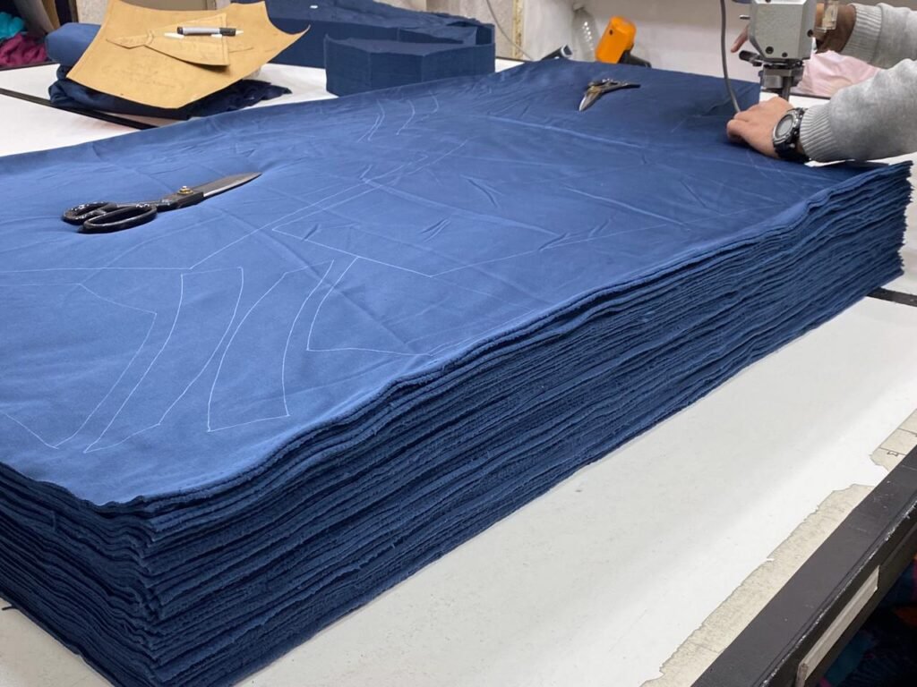 Layers of navy fabric marked with garment patterns and prepared for cutting.