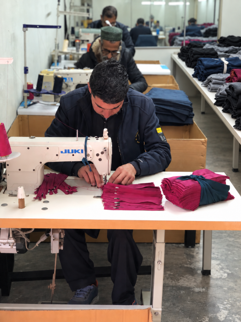 Workers sewing magenta garment panels on an industrial sewing machine.